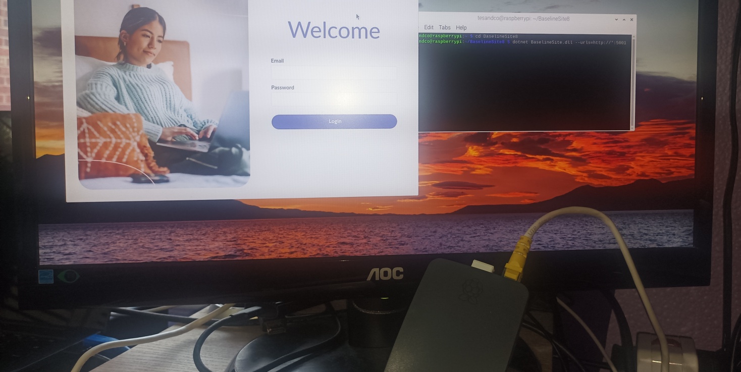Cropped image showing a monitor and a Raspberry Pi. The monitor shows the Raspberry Pi OS desktop with a browser running Umbraco 13.